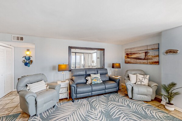 A living room with a grey sofa, two armchairs, a patterned rug, and wall art.