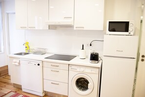 A compact kitchen with a dishwasher, washing machine, microwave, and a small countertop with a sink and a kettle.