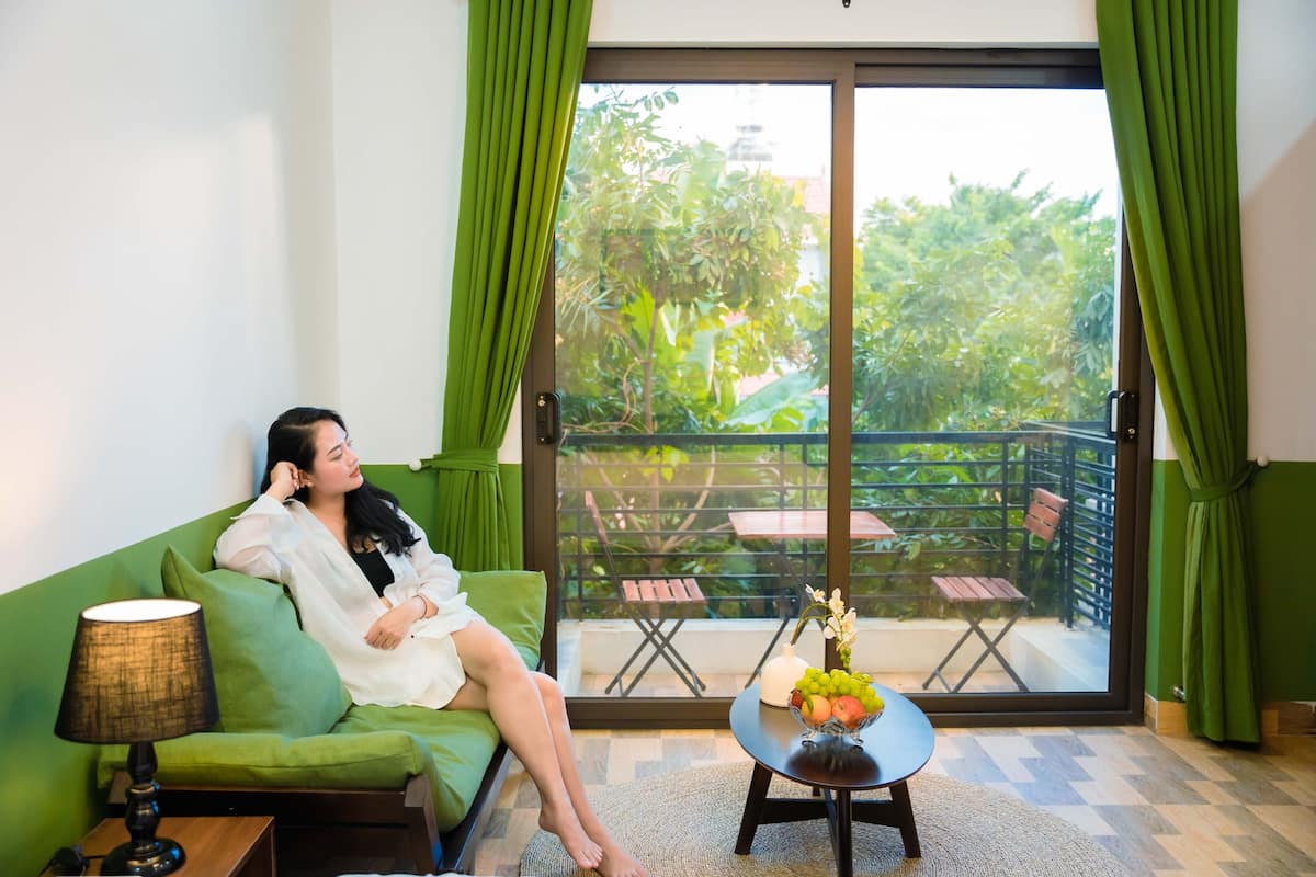 Une pièce avec un canapé vert, une petite table sur laquelle se trouve un panier de fruits, et une vue sur un balcon aménagé avec du mobilier d’extérieur.