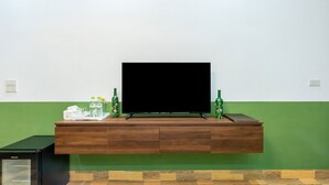 Un salon moderne avec un téléviseur à écran plat posé sur une console en bois, un mini-réfrigérateur et des bouteilles décoratives.