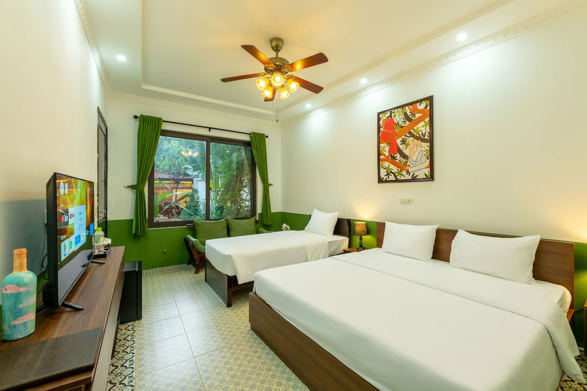 Une chambre d’hôtel avec deux lits simples, un ventilateur de plafond, une télévision et une fenêtre avec des rideaux verts.