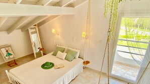 Quarto com cama, cadeira suspensa, janela com vista para o verde e uma porta.