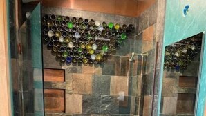 A bathroom with a glass shower enclosure, a sink with a mirror, and a tiled wall with a unique bottle arrangement. - Unique studio with cozy patio (La Mesa)