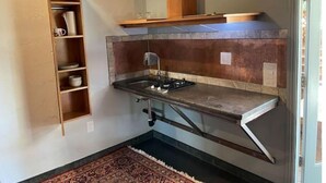 A compact kitchen with a built-in stove, a wooden shelf, and a small countertop. - Unique studio with cozy patio (La Mesa)