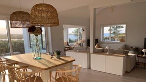 Un vaste espace dédié à la salle à manger, avec une table et des chaises en bois, une grande fenêtre offrant une belle vue et un coin salon confortable avec un canapé et des lampes.