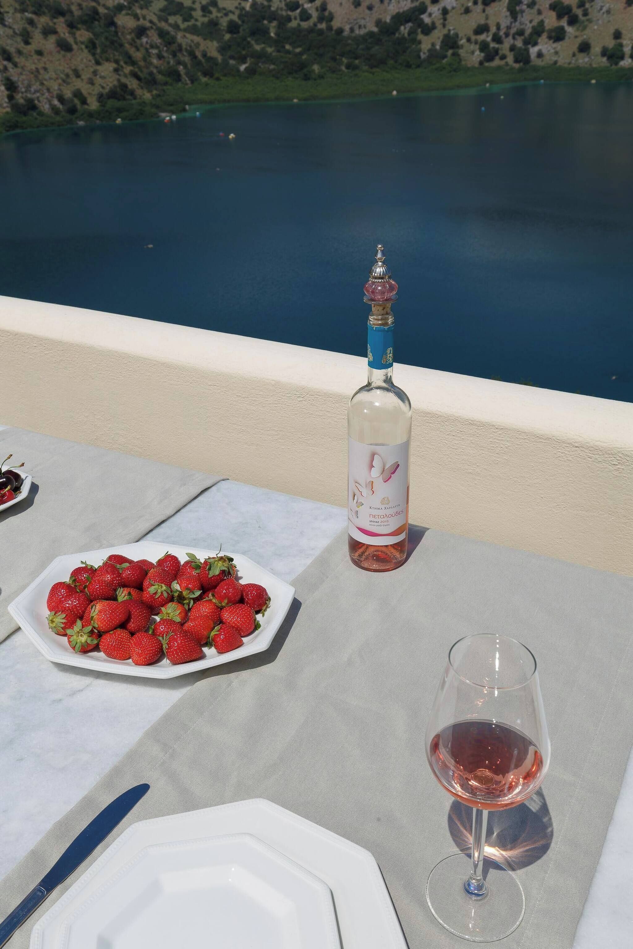 A table with a bottle of wine, a glass of wine, and a plate of strawberries.