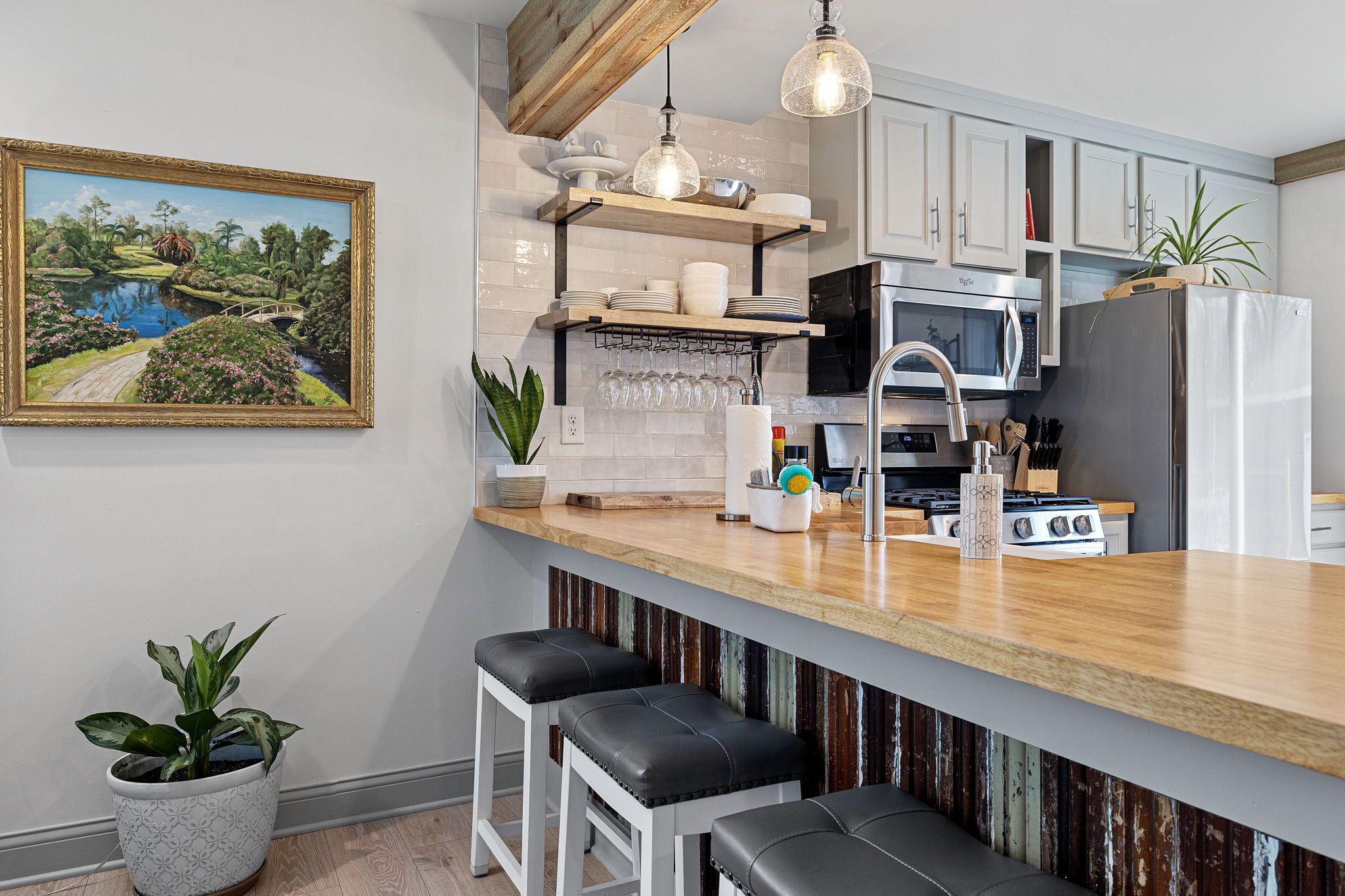 Une cuisine moderne dotée d’un plan de travail en bois, d’appareils électroménagers en acier inoxydable et d’un luminaire suspendu.