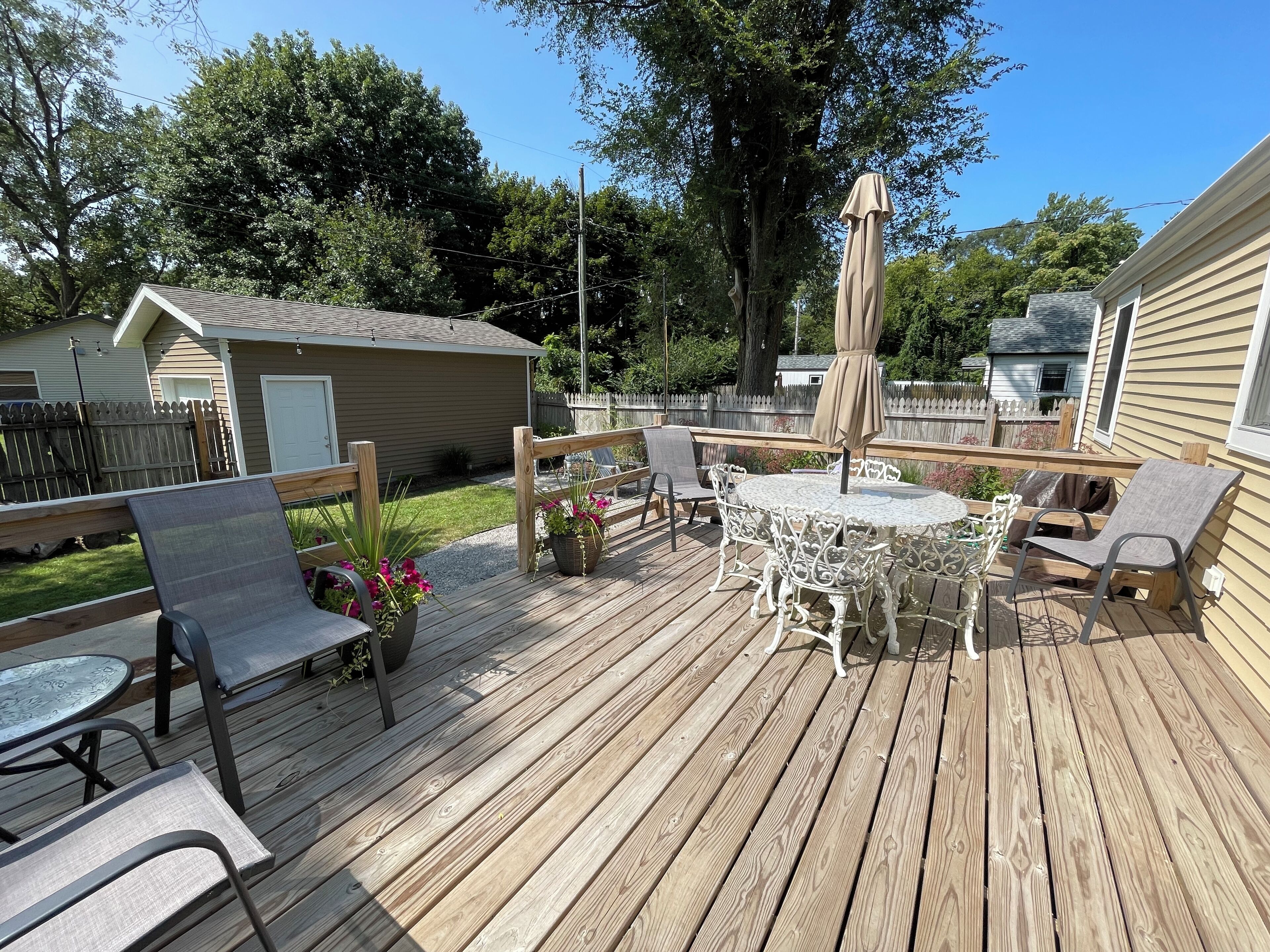 A wooden deck with outdoor furniture, including chairs and a table, surrounded by a wooden fence and trees.