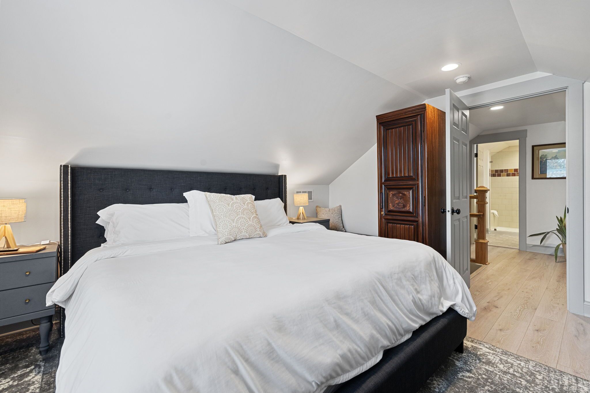 Un dormitorio con una cama grande, una mesita de noche, un armario de madera y una puerta que da al baño.