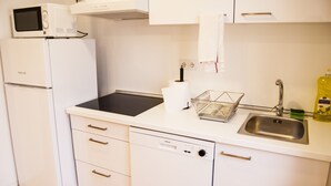Una cucina compatta con un frigorifero bianco, un forno a microonde, una lavastoviglie, un lavello e un piccolo piano di lavoro con un bollitore e un erogatore di sapone.