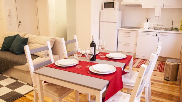 Zona pranzo con tavolo apparecchiato per quattro, un forno a microonde e un frigorifero sullo sfondo.