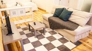 Una camera d'albergo moderna con un tappeto a scacchi, un divano con cuscini, una TV su un tavolino e un armadio.