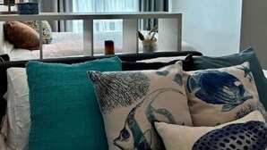 A modern living room with a sofa set, a coffee table, and a window with curtains. - CityScape Condo: Vibrant & Central BGC (Taguig)