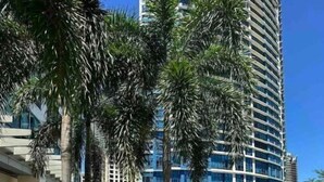A hotel with a swimming pool, palm trees, and a modern building in the background. - CityScape Condo: Vibrant & Central BGC (Taguig)
