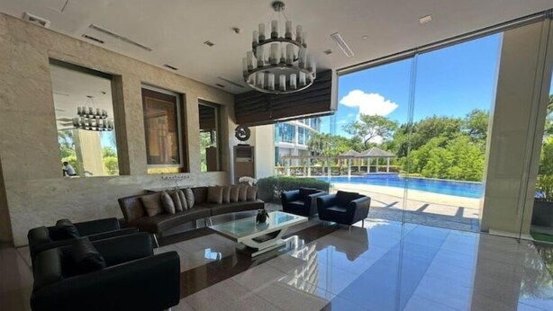 A modern living room with a large glass door leading to a pool, a sofa set, and a chandelier. - CityScape Condo: Vibrant & Central BGC (Taguig)