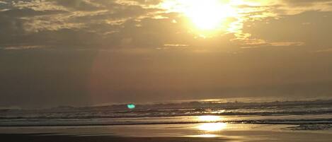 A beach with the sun setting over the horizon, creating a silhouette of the landscape.