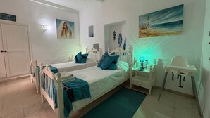 A bedroom with two beds, a white wardrobe, a small table with a lamp, and a painting of a beach scene. - Dar Lola (Houmt Souk)