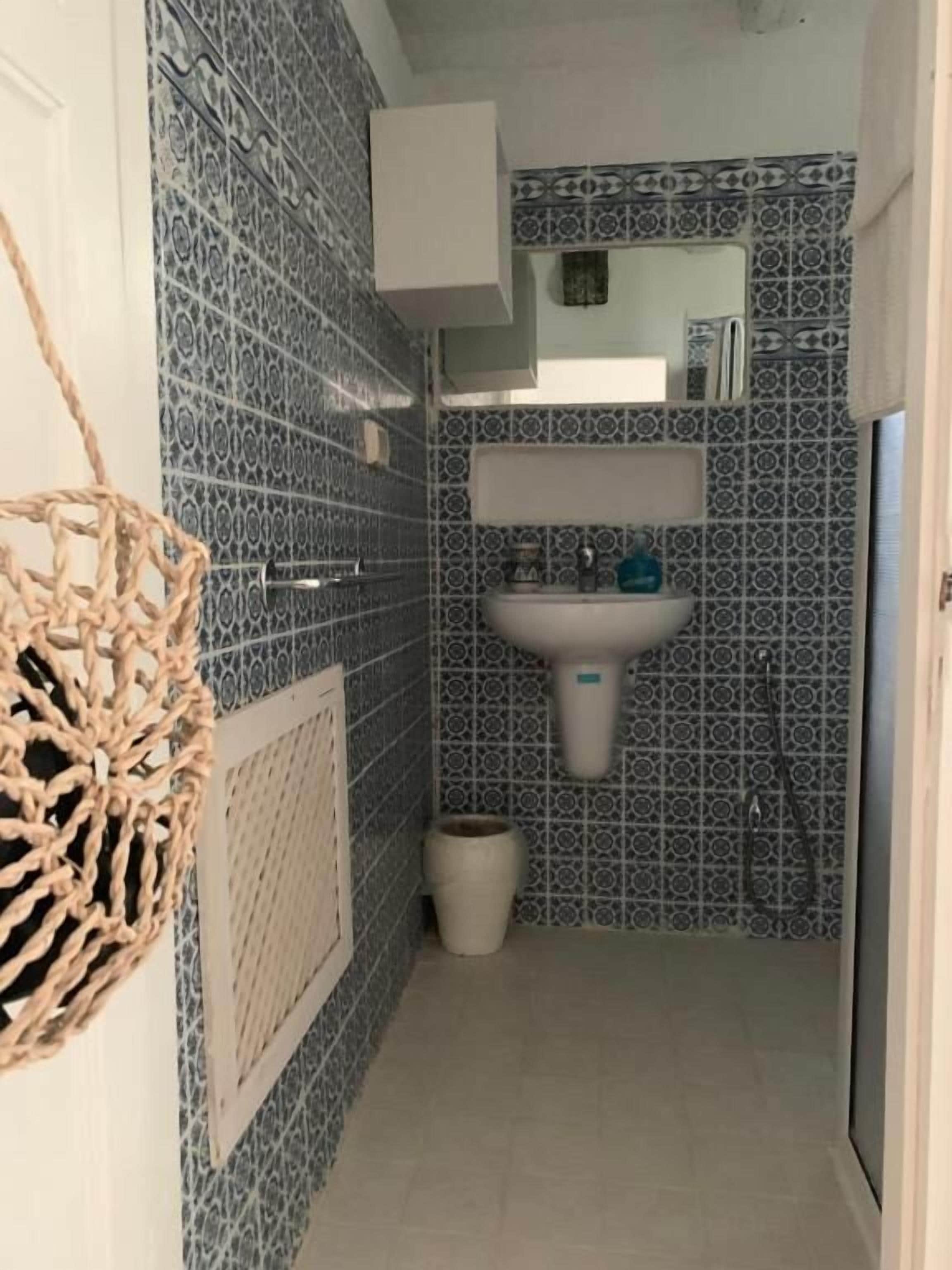Un baño con baldosas estampadas, un lavabo, un espejo y una cesta colgante.