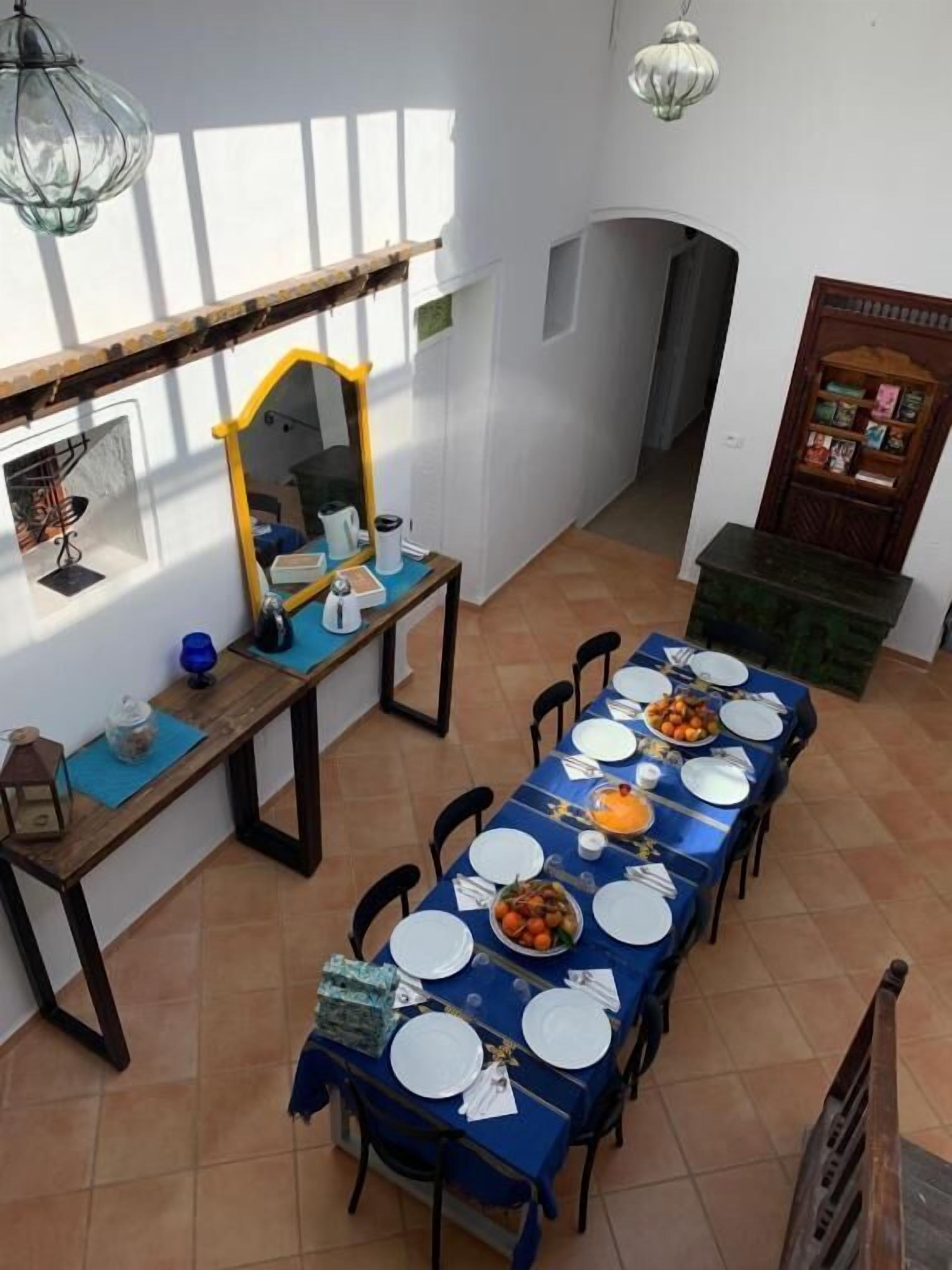 A dining area with a long table set for a meal, a mirror, and a shelf with books.