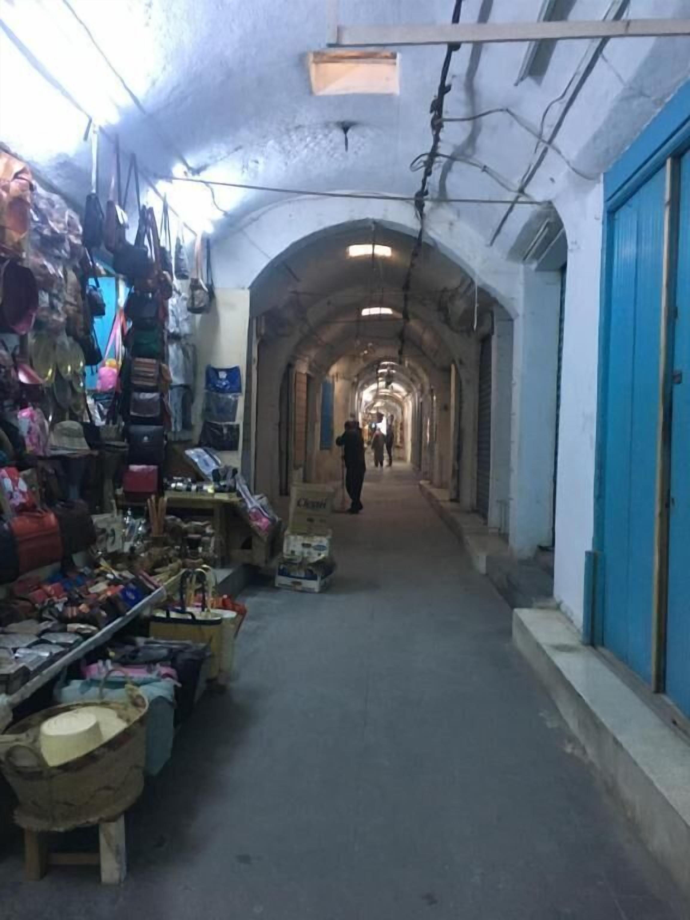Un marché couvert avec une allée centrale, divers étals de chaque côté et une porte bleue au fond.
