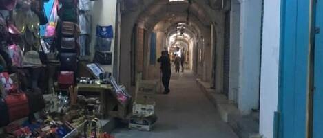 An indoor market with a central aisle, various stalls on either side, and a blue door at the end.