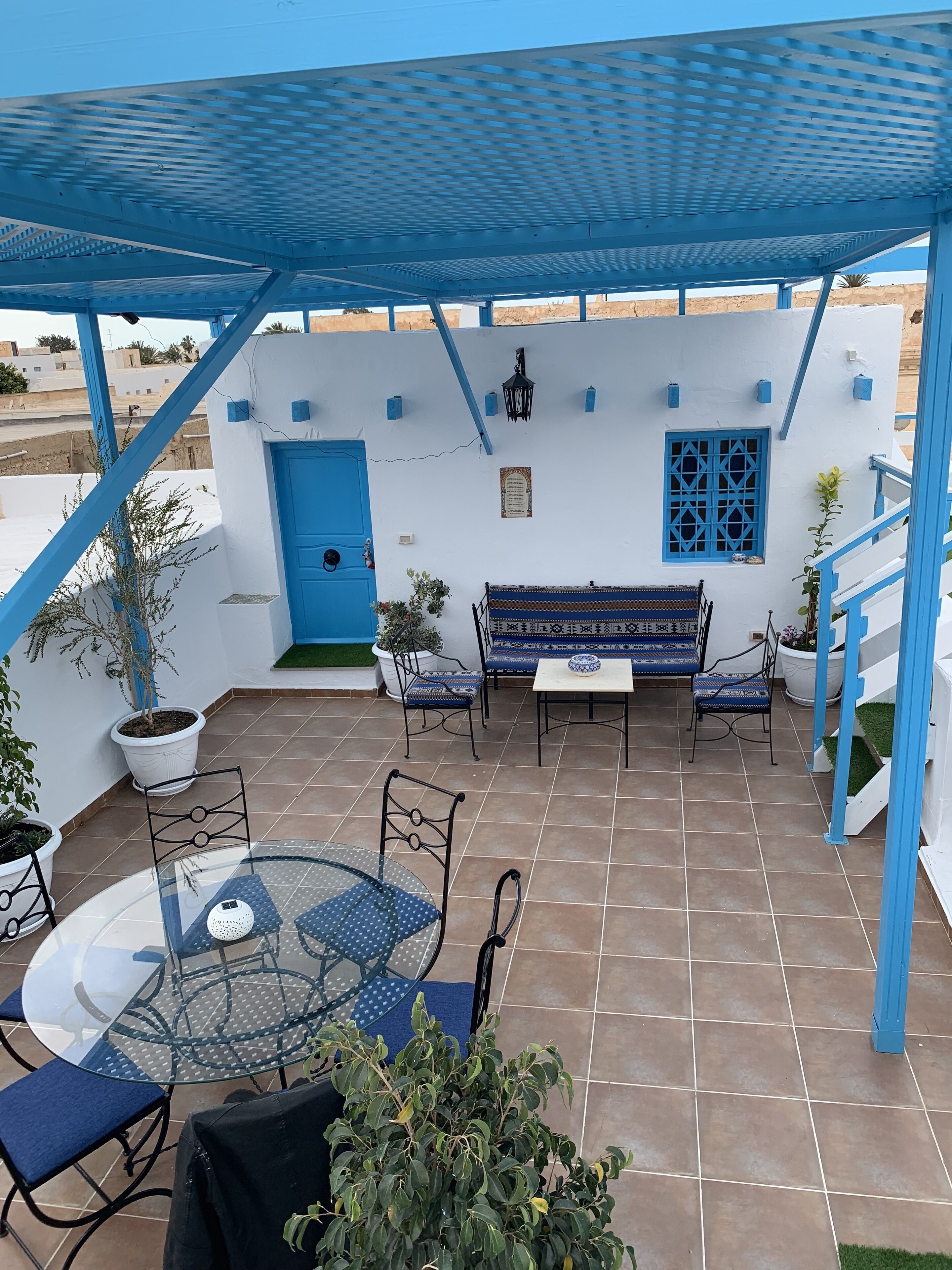 Un espace extérieur abrité, doté d’un toit bleu, de murs blancs et d’un sol carrelé.