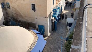 Une rue étroite, bordée de bâtiments des deux côtés, dont certains sont dotés d'auvents bleus et quelques-uns arborent des enseignes bien visibles.