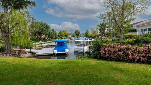 A canal with boats docked, surrounded by greenery and a residential area. - Serene Lake Retreat (Westlake Village)