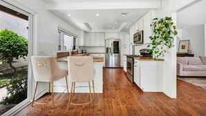 A modern kitchen with white cabinetry, a central island, and a dining area with two chairs. - Serene Lake Retreat (Westlake Village)