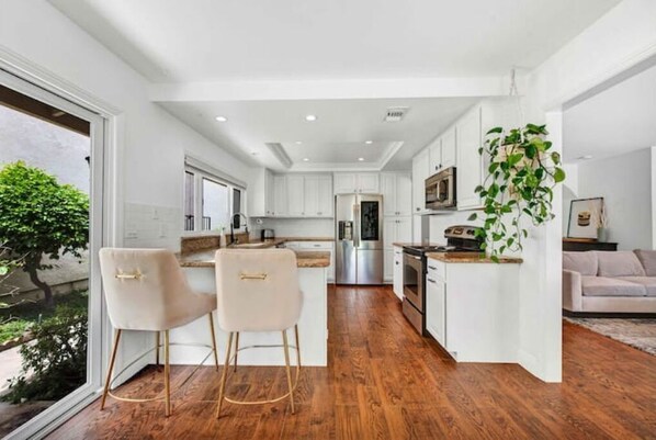 A modern kitchen with white cabinetry, a central island, and a dining area with two chairs.