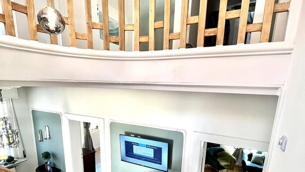 A multi-level interior with a wooden staircase, a flat-screen TV mounted on the wall, and a seating area with a green chair. - Old villa in the heart of Lorsch (Lorsch)