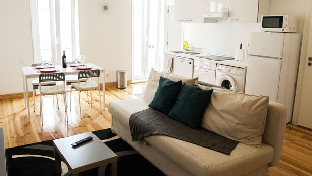 Una sala moderna con un sofá, un comedor con sillas y una mesa, y una cocina con electrodomésticos.