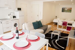 Eine moderne, gut beleuchtete Wohnung mit Essbereich, Küchenzeile und Wohnbereich mit Sofa und Fernseher.