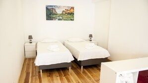 Una habitación con dos camas, suelo de madera, paredes blancas y un cuadro de un paisaje.
