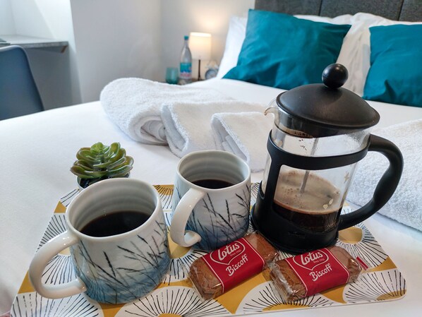 Un plateau de petit-déjeuner soigneusement préparé est posé sur le lit, avec une machine à café, deux tasses de café et deux biscuits Lotus.