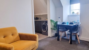 Una sala de estar moderna con un sofá amarillo, una zona de comedor con mesa y sillas, y una cocina al fondo.