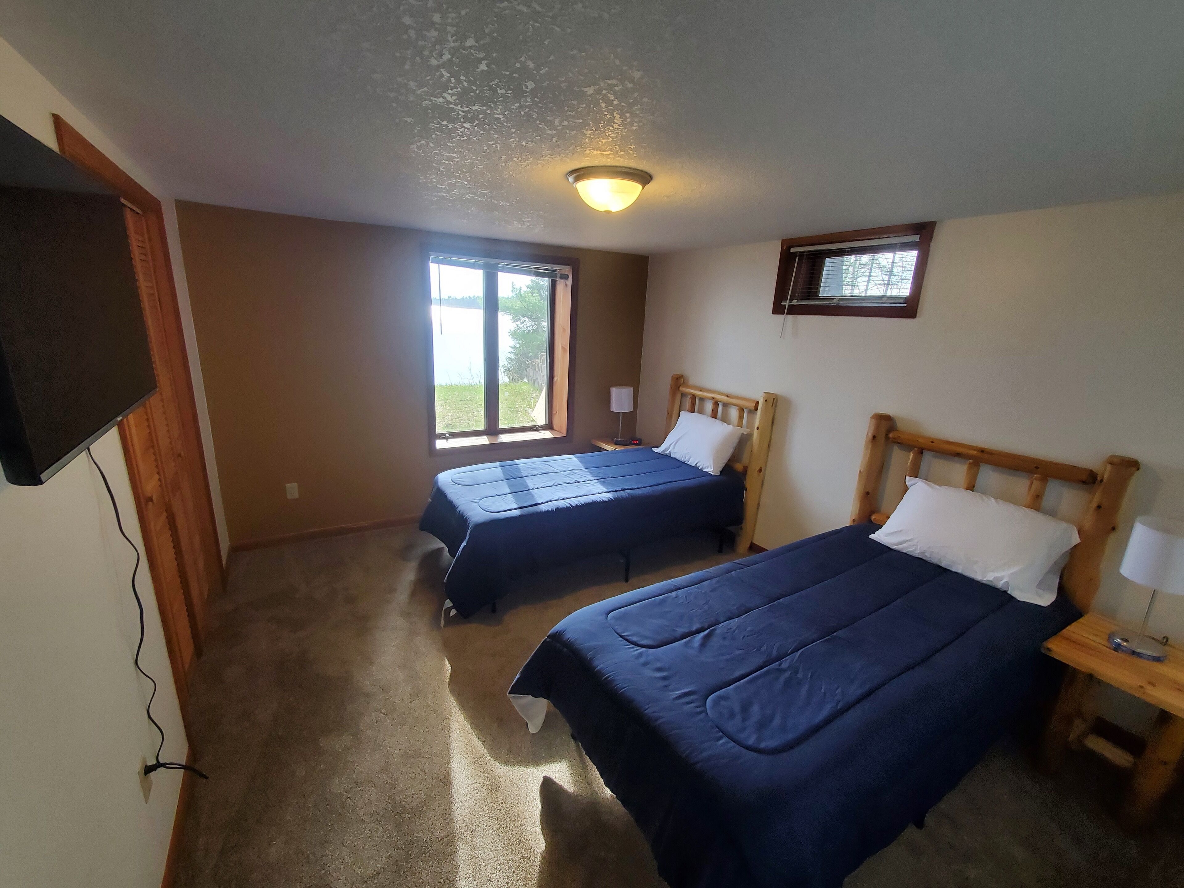 Un dormitorio con dos camas, una lámpara en el techo, una ventana y un televisor montado en la pared.