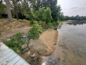 Enjoy serene lake views from the deck, leading to a sandy beach area with a staircase.
