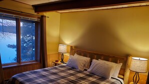 Un dormitorio con una cama grande, dos lámparas de noche, una mesita de noche y una ventana con vista a árboles.