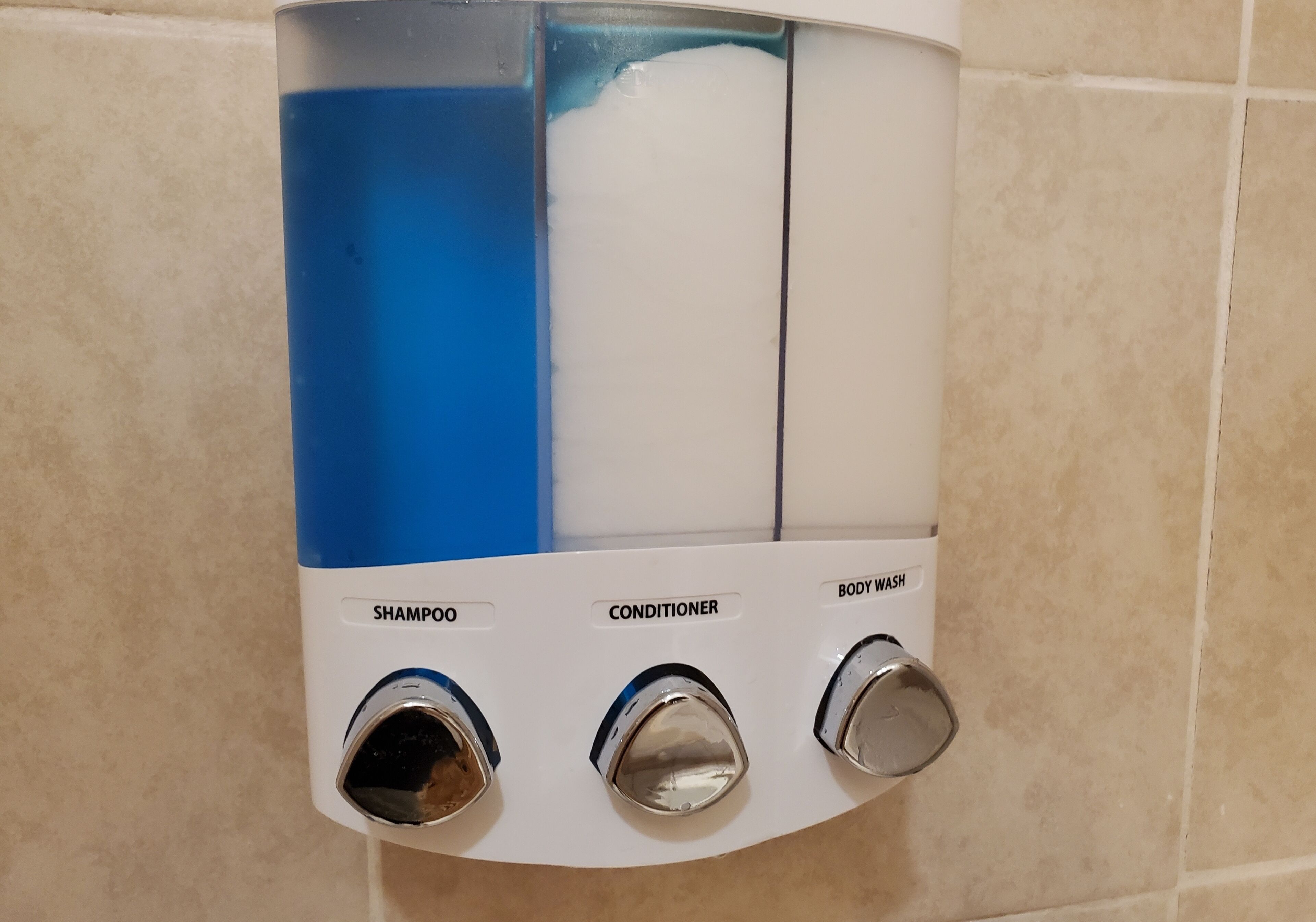 Dispensador empotrado en la pared con tres salidas etiquetadas para champú, acondicionador y gel de ducha.