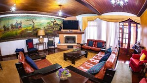 A spacious living room with a fireplace, leather sofas, a large painting, and a television. - Colônia de Férias SAA (Campos do Jordão)