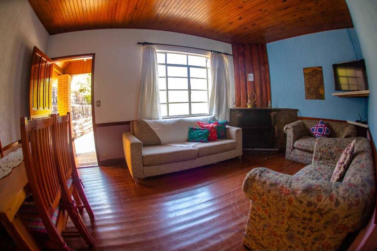 A cozy living room with a wooden ceiling, a sofa, a patterned armchair, and a television.