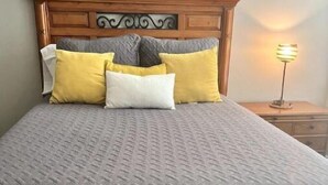 A neatly made bed with a wooden headboard, a gray quilt, and three pillows in yellow and white. - Cowtown 1 bedroom in Downtown FT Worth (Fort Worth)