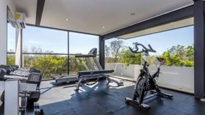 Un gimnasio moderno con equipo de ejercicio, ventanas amplias y vistas a zonas verdes.