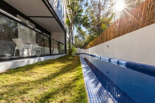 A modern outdoor swimming pool with a glass enclosure, surrounded by a grassy area and a wooden fence.