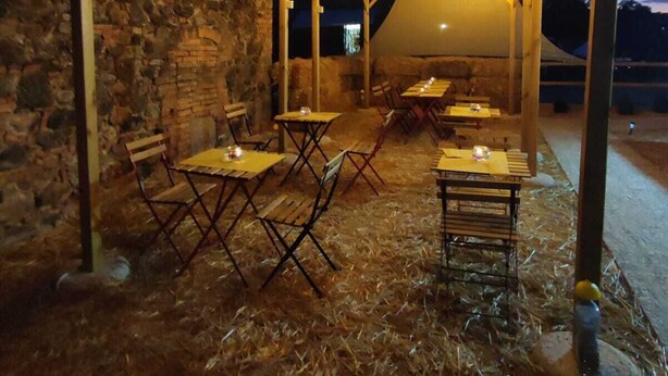 Un espace extérieur aménagé en terrasse, avec des tables et des chaises sous une pergola en bois, le tout entouré de murs en pierre.