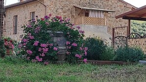 Une maison en pierre dotée d’un petit balcon, entourée d’un jardin où poussent des fleurs roses.