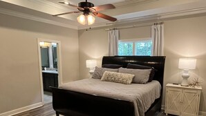 Un dormitorio con cama, ventilador de techo, mesita de noche y ventana con cortinas.
