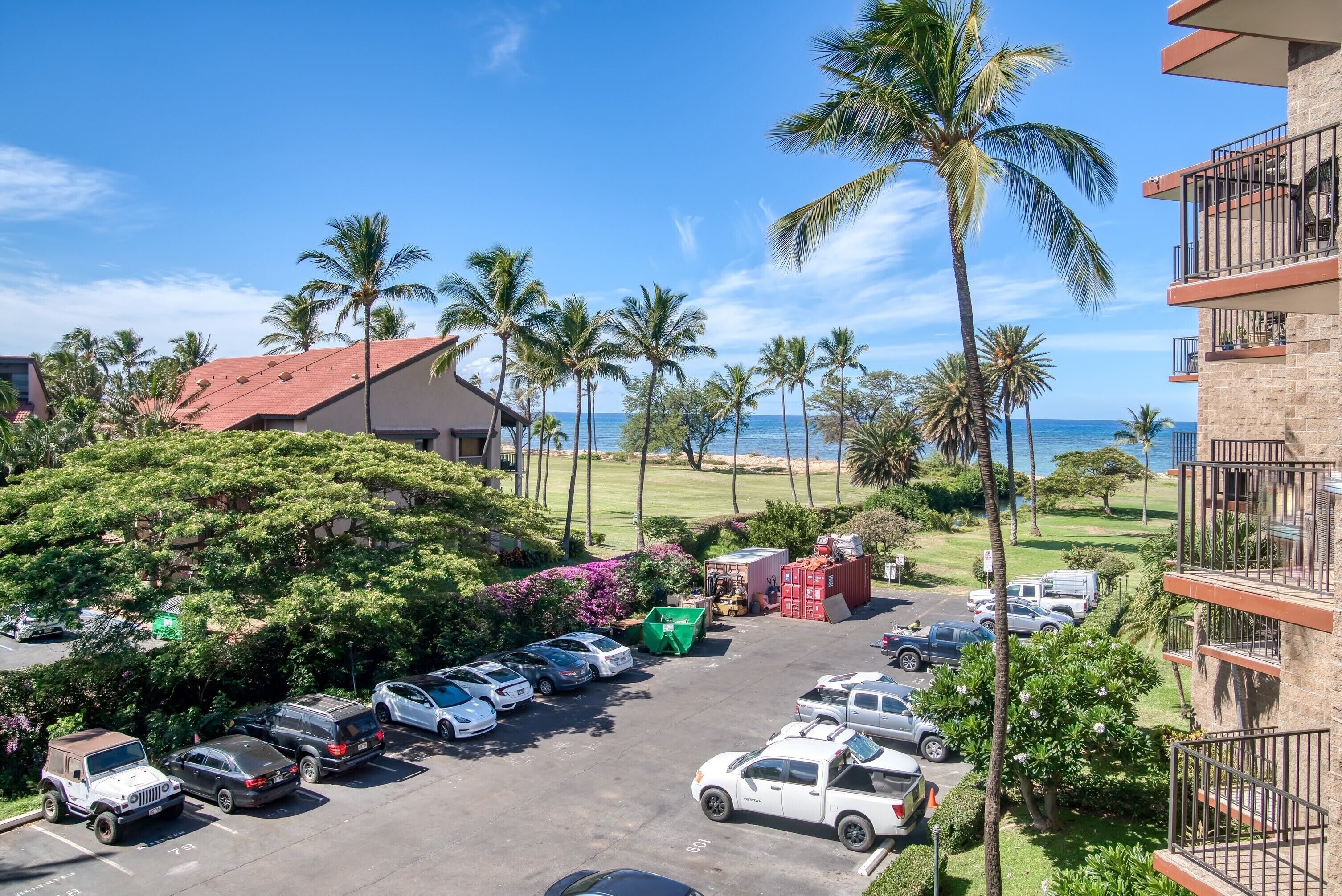 A parking lot with various cars, a building with a red roof, and palm trees.