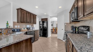 Una cocina moderna con encimeras de granito, armarios de madera oscura, un refrigerador de acero inoxidable y una zona de comedor al fondo.